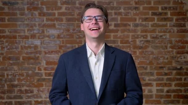 Chill caucasian businessman is laughing next to camera in motion standing in same position, brick background — Stock Video