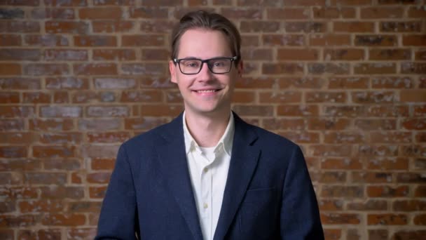 Happy caucasian businessman in glasses demonstrating like gesture and looking at camera straight, brick wall behind — Stock Video