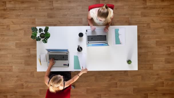 Top shot dos mujeres están trabajando mientras están sentados uno al lado del otro en la mesa centrada en el proceso de trabajo, utilizando computadoras portátiles — Vídeo de stock