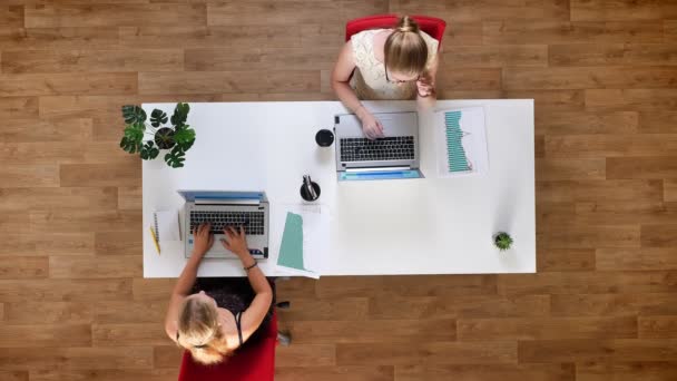 Top shot, dos colegas mujer usando theis dispositivos de trabajo, desplazamiento en las computadoras portátiles concenrated — Vídeo de stock