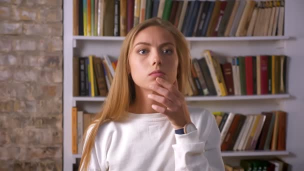 Pensando mujer caucásica concentrada en sus mentes de pie en la biblioteca, aspecto hermoso — Vídeo de stock