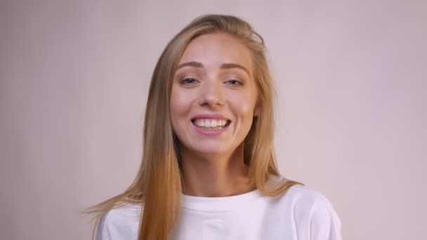 Светлая смеющаяся блондинка с длинными волосами, смотрящая на камеру расслабленной в белой студии — стоковое видео