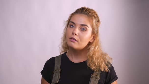 Jistý docela kavkazské dívka na bílém pozadí ve studiu při pohledu na fotoaparát a kouše se do rtů vážně — Stock video