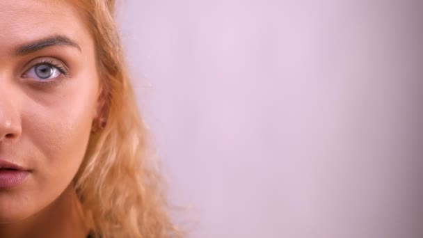 Close-up focused half face of the pretty caucasian blonde female looking at camera calm and chill on white background — Stock Video