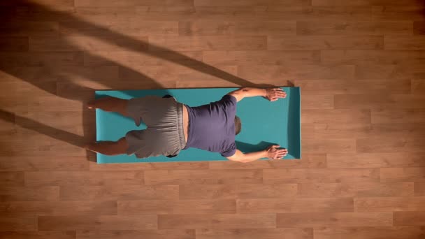 Top shot, Kaukasisch mannetje maakt verschillende asana's binnen en joga indoor gelet op een blauwe mat, geconcentreerd met ogen dicht — Stockvideo