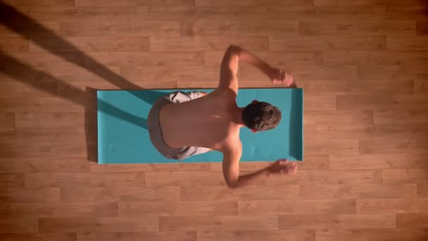 Top shot, sportlicher kaukasischer Rüde wird von Yogamatten abgetrennt und steht gerade auf Holzboden im Innenraum — Stockvideo