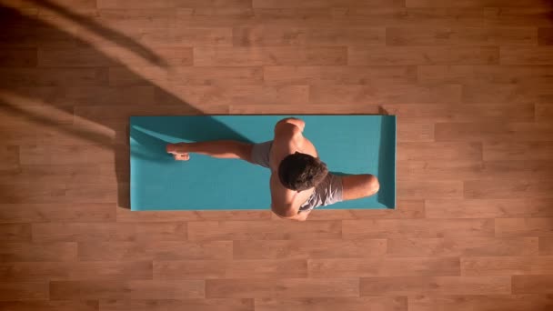 Сверху вниз, белый красивый мужчина держит равновесие стоя на одной ноге, согнутой на колене, глядя прямо на коврик Joga внутри — стоковое видео