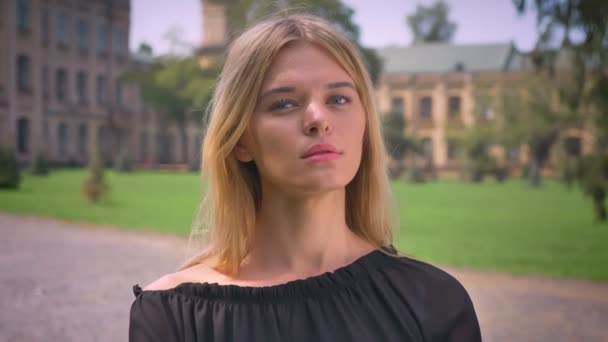 Confident caucasian short-haired blonde female is looking straight at camera, standing on the street calm — Stock Video