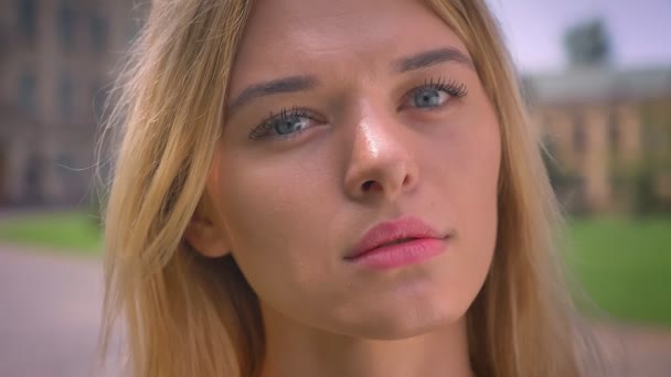 Nahaufnahme des konzentrierten Gesichts einer hübschen kaukasischen blonden Frau, die ernst schaut, während sie draußen in der Nähe von Gebäuden steht — Stockvideo