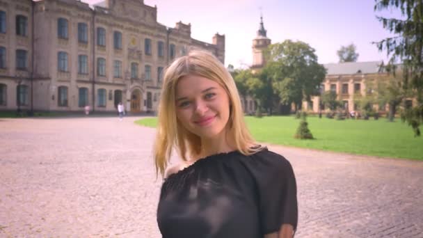 Menina loira branca impressionante em movimento no fundo da cidade e demonstrando como gesto com sorriso bonito ao ar livre — Vídeo de Stock