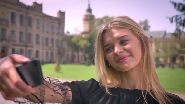 Picky sorriso alegre de mulher caucasiana que leva selfie e fica na rua perto do parque, dia ensolarado — Vídeo de Stock