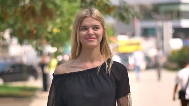 Mulher caucasiana feliz está parado e sorrindo para a câmera, olhando para o lado, olhando em linha reta novamente, fundo ensolarado urbano — Vídeo de Stock