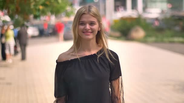 De pé mulher loira caucasiana que está sorrindo feliz para a câmera, não se movendo na rua, humor da cidade — Vídeo de Stock