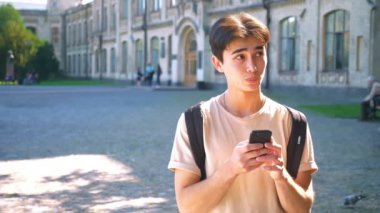 Gülen mutlu Asya'ya ait adam onun smartphone, iletişim, kullanarak sokak ayakta, kentsel mood, rahat güneşli yer