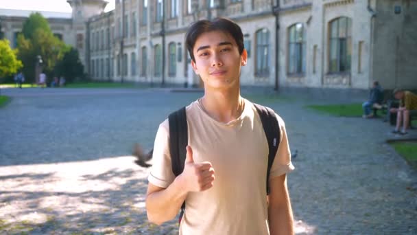 Calm and confident asian man is showing like sign while standing on the street in sunlights with old building on background — Stock Video