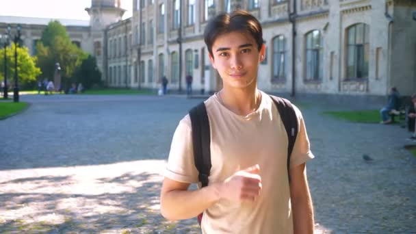 NIce asiático menino está demonstrando como gesto enquanto em pé em linha reta na rua vazia, sol brilha rodeia vista — Vídeo de Stock