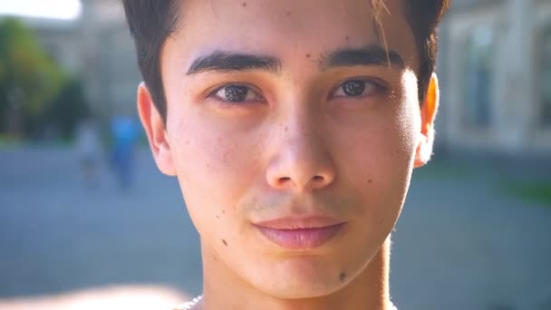 Bonito asiático homem close-up sorrindo em aparelho e olhando para a câmera relaxada, humor frio, fora, raios de sol — Vídeo de Stock