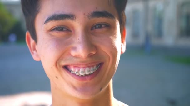 Hermosa asiático feliz chico es riendo en brackets y mirando a un lado, mientras de pie en la calle — Vídeo de stock