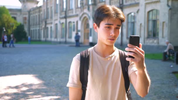 Angenehmer Asiatischer Mann Telefoniert Benutzt Webkamera Steht Vor Dem Universitätsgebäude — Stockvideo