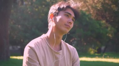Güzel Asyalı erkek çimde oturma ve müzik chill, açık, park manzaralı ritim içinde hareket