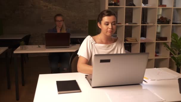 Hermosas chicas colegas caucásicos, sentado frente a las computadoras portátiles y escribir centrado, estado de ánimo de trabajo, oficina de ladrillo — Vídeos de Stock