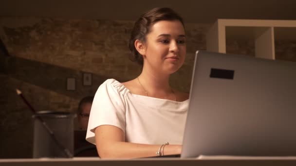 Focused pretty caucasian businesswoman is using laptop while sitting next to other colleague in brick studio — Stock Video