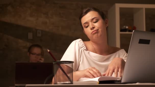 Stufo donna caucasica è seduto alla scrivania con sguardo annoiato e utilizzando computer portatile al coperto — Video Stock