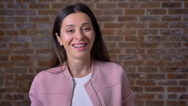 Happy look de femme brune caucasienne, souriant gentiment à la caméra debout près du mur de briques intérieur — Video