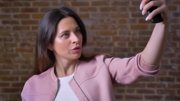 Awesome Kaukasische vrouw is opknoping op de video-oproep, haar telefooncamera kijken en praten chill, rode bakstenen achtergrond — Stockvideo