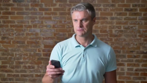 年配の白人男性は、携帯電話で入力して赤いスタジオだけに立って冷静に焦点を当ててください。 — ストック動画
