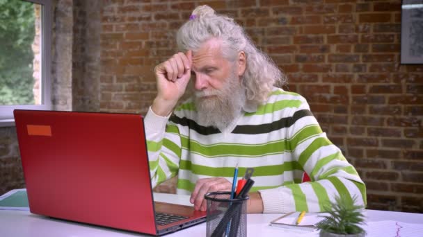 Orang tua Kaukasia yang menyenangkan dengan jenggot putih tebal mengetik di komputernya berkonsentrasi, terlibat dalam proses kerja, kantor bata — Stok Video