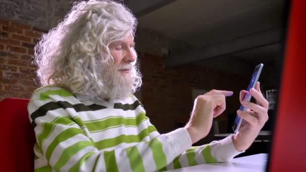 Schattig Kaukasische oma met mooie witte baard en haren is weergegeven: blauw scherm op tablet, ontspannen en rustig, baksteen achtergrond afbeelding — Stockvideo