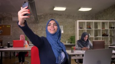 Heppy Arap kadın ona telefon diğer Müslüman kızlar, modern iş kadınları ile tuğla ofis sandalyede otururken selfie alıyor