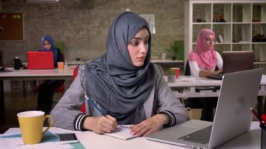 Şaşırtıcı İslam kız notlar ve sakin bir şekilde bilgisayar başında, vasıl okul sırası, otururken arka plan üzerinde Arapça kız arıyorum