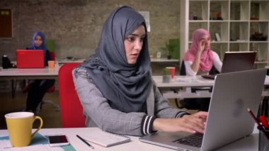 Esneme yorgun güzel Arap kız Masaüstü, arka plan, modern bayanlar, hafif tuğla ofis meslektaşları, otururken laptopunu kullanıyor
