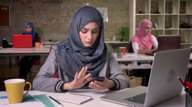 Güzel Arap erkek onun smartphone, çalışma ortamı swiping, laptop üzerinde arka plan ar oturma Müslüman kızlar açık ve dizüstü bilgisayarlar, kullanarak office tuğla