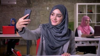 Muhteşem Arap gri hijam alır selfies onun smartphone üzerinde çalışma, arka plan tuğla illüstrasyon iş arkadaşları kızlar işyerinde, otururken kadındır.