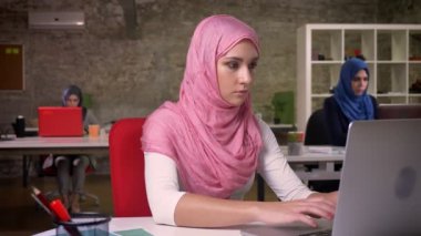 Yakışıklı Müslüman erkek pembe güzel hijab bilgisayarda yazarak konsantre, masaüstünde, arkasında, modern iş çalışan Arap kadın oturuyor