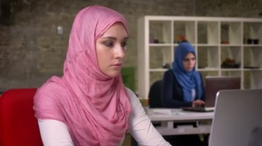 Pembe hijab harika Arap kadın tuğla ışık ofisinde oturan ve meslektaşları hijabs işlerine konsantre arka plan üzerinde çalışma bilgisayarını kullanarak