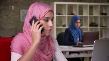 Kendine güvenen güzel Müslüman kız odaklı olan telefon konuşmak tüm onun kafasında kendi masaüstlerinde Arapça diğer kızlarla tuğla ofisinde otururken, modern yaşam tarzı