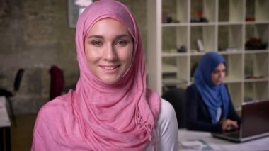 Sevimli gülümseme ile pembe hijab ayakta, ofis çalışma ruh, tuğla stüdyo kapalı, Ortadoğu vibes Müslüman kadın