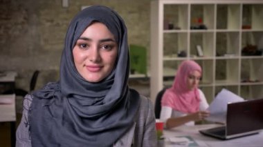 Gri hijam Müslüman kadın yakın çekim güzel yüzü olurken doğrudan kameraya baktığımda onun meslektaşları İslam çalışma ruh tarafından çevrili tuğla ofis