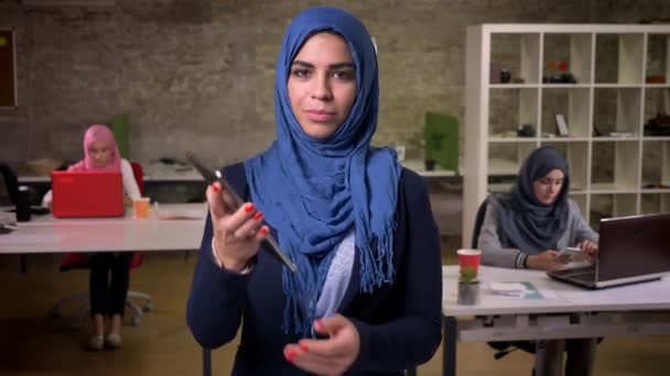 Söt trevlig kvinna i blå hijab visar blå skärm och innehav tablett bara på kameran, stående i tegel ljus kontor nära andra Mellanöstern flickor — Stockvideo