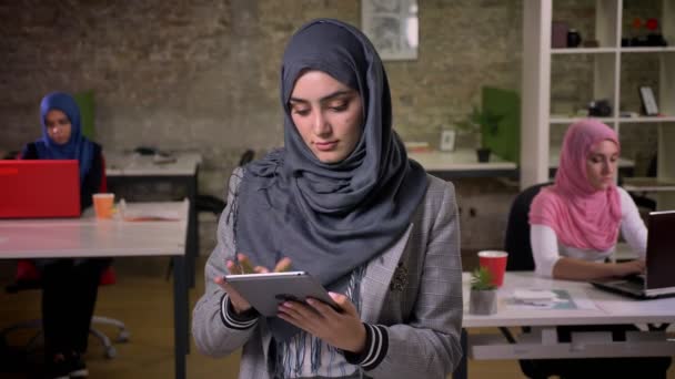 Korku veren gülümseyen Arap kadın gri hijab gösteri yeşil ekran onun tablet üzerinde kapalı, ayakta iken kadın nsitting kendi işyerleri, tuğla arka plan çalışma mı — Stok video