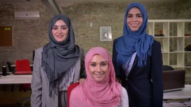 Üç Arap kadınlar ar ayakta kamera yakın ve cwith güven, tuğla içinde farklı hijab giyen seyir gülümseyen office ışık