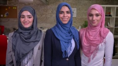 Güzel üç Arap hijab kız birlikte ürpertiyle bekliyoruz emin gülümseyen yüzler, kamera konsantre tuğla stüdyo içine bakmak