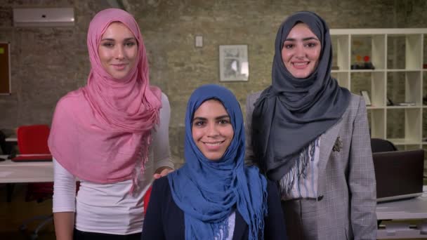 Enjouable meninas muçulmanas ar olhando para a câmera em hijab de cores rosa, cinza e azul, fundo de tijolo moderno, ilustração de trabalho — Vídeo de Stock