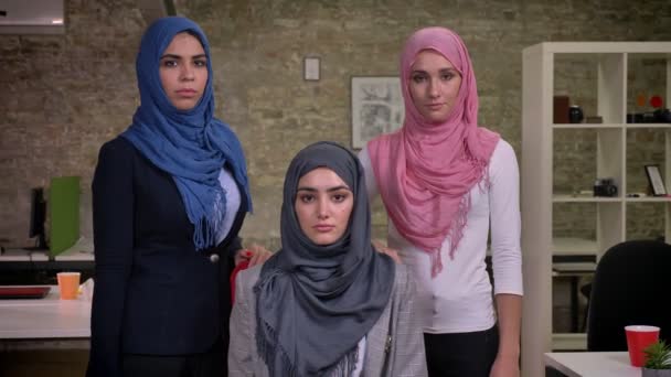 Sério três árabe mulheres ar olhando diretamente para a câmera vestindo hihab, vibrações de trabalho do Oriente Médio, tijolo escritório moderno interior — Vídeo de Stock