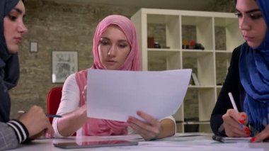 Pembe hijab güzel Arap kadını iş belgeleri, birlikte ortak masada oturan tutan diğer Müslüman kadınlarla konuşmayı