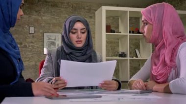Şirin çalışan Arap türban kadın konsantrasyonu ve ortak Danışma, oturma, farklı iletişim, tuğla arka plan kapalı tartışma vardır